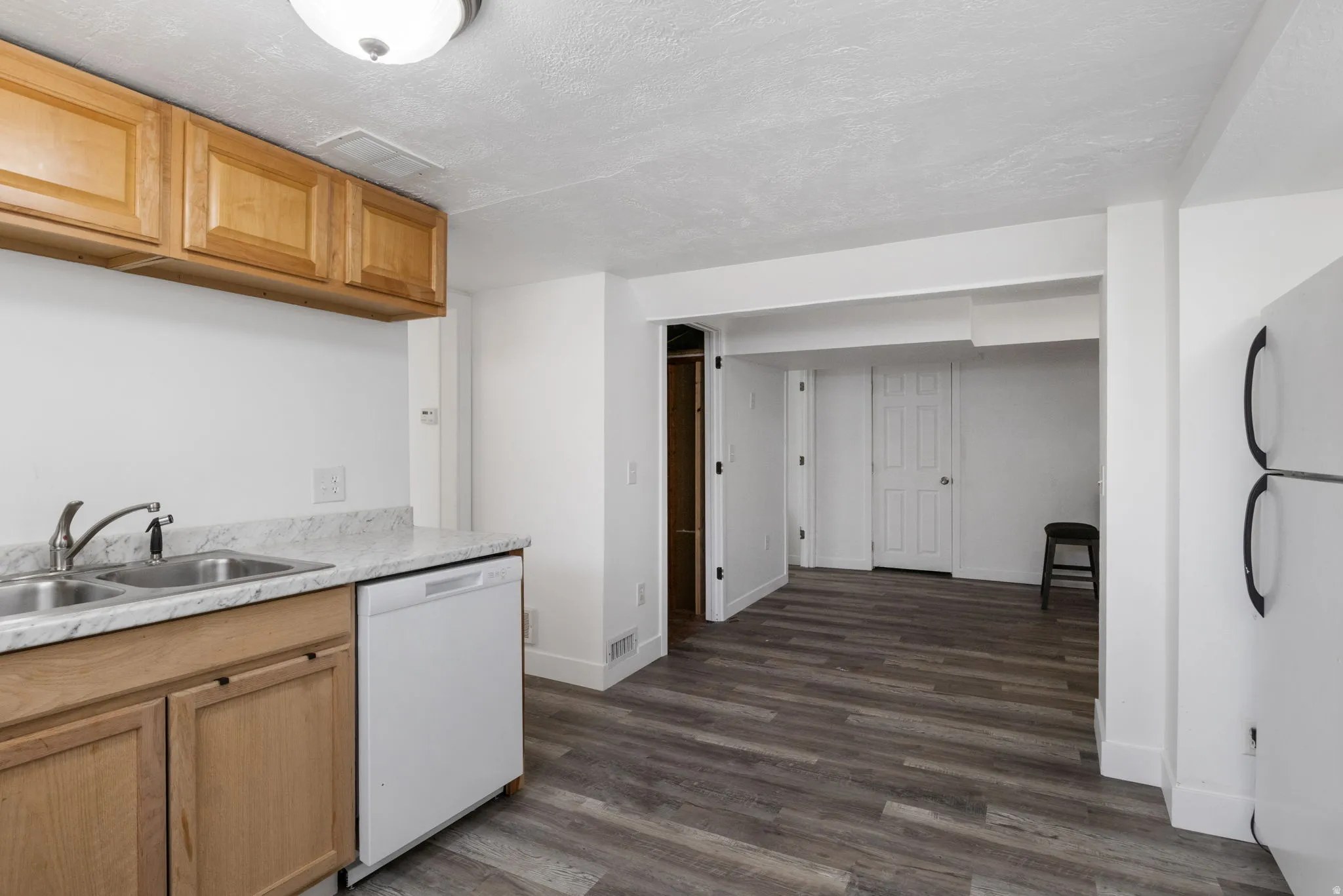 Kitchen with light countertops, dishwasher, freestanding refrigerator, dark vinyl floors, and a textured ceiling