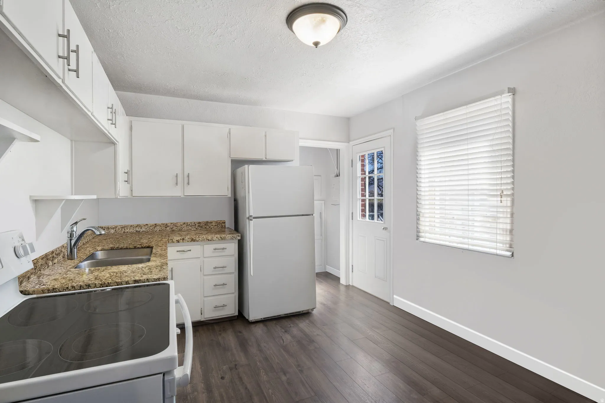 Kitchen with white appliances, white cabinetry, dark wood-style floors, a textured ceiling, and light stone countertops