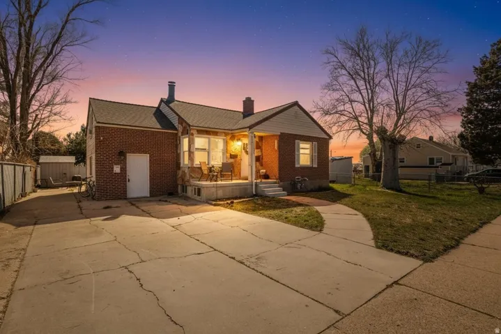 View of front of home featuring a chimney, brick siding, driveway, and a patio