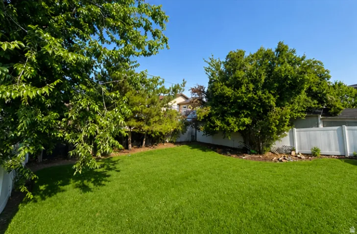 Expansive green lawn with mature perimeter trees and shrubs, bordered by white privacy fencing