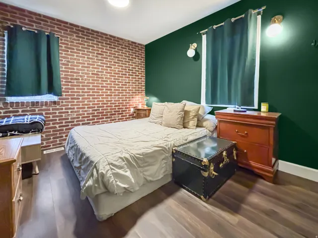 Bedroom featuring an accent wall, brick wall, and dark wood finished floors