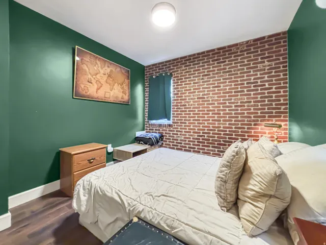 Bedroom with brick wall, an accent wall, and dark wood-style flooring
