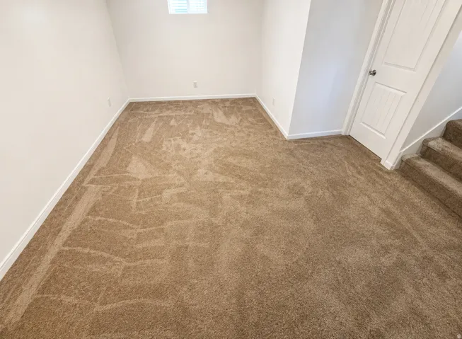 Neutral tone carpet flooring, white painted walls, white trim, paneled door, and a window providing natural light