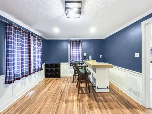 Home office with a wainscoted wall, a decorative wall, light wood finished floors, a textured ceiling, and crown molding