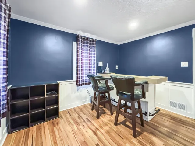 Dining room with light wood-type flooring, a wainscoted wall, a decorative wall, and ornamental molding