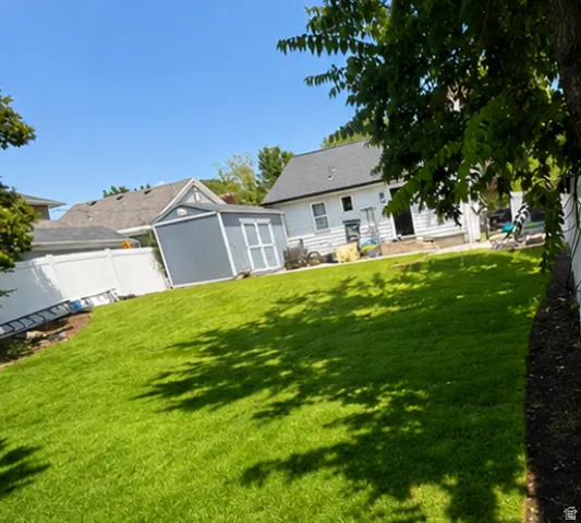 Expansive lawn area with a white vinyl privacy fence and an outbuilding