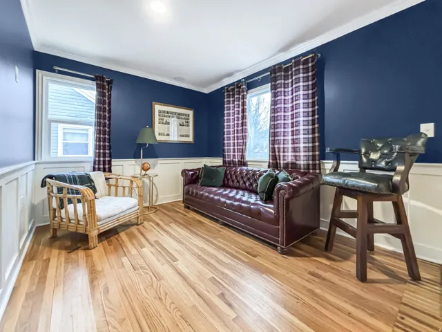 Living room featuring wainscoting, light wood-style flooring, crown molding, and a decorative wall