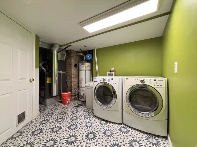 Laundry area featuring secured water heater, heating unit, washing machine and dryer, and light floors
