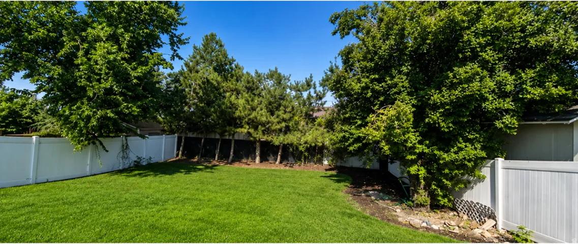 Expansive private yard featuring a substantial lawn, mature trees, and a durable panel fence
