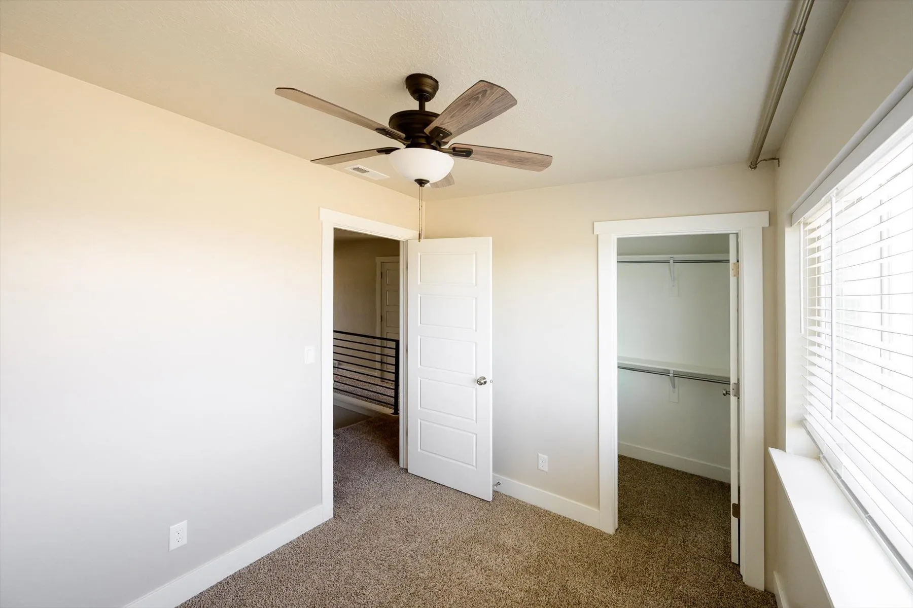 Unfurnished bedroom with dark carpet, a walk in closet, and ceiling fan