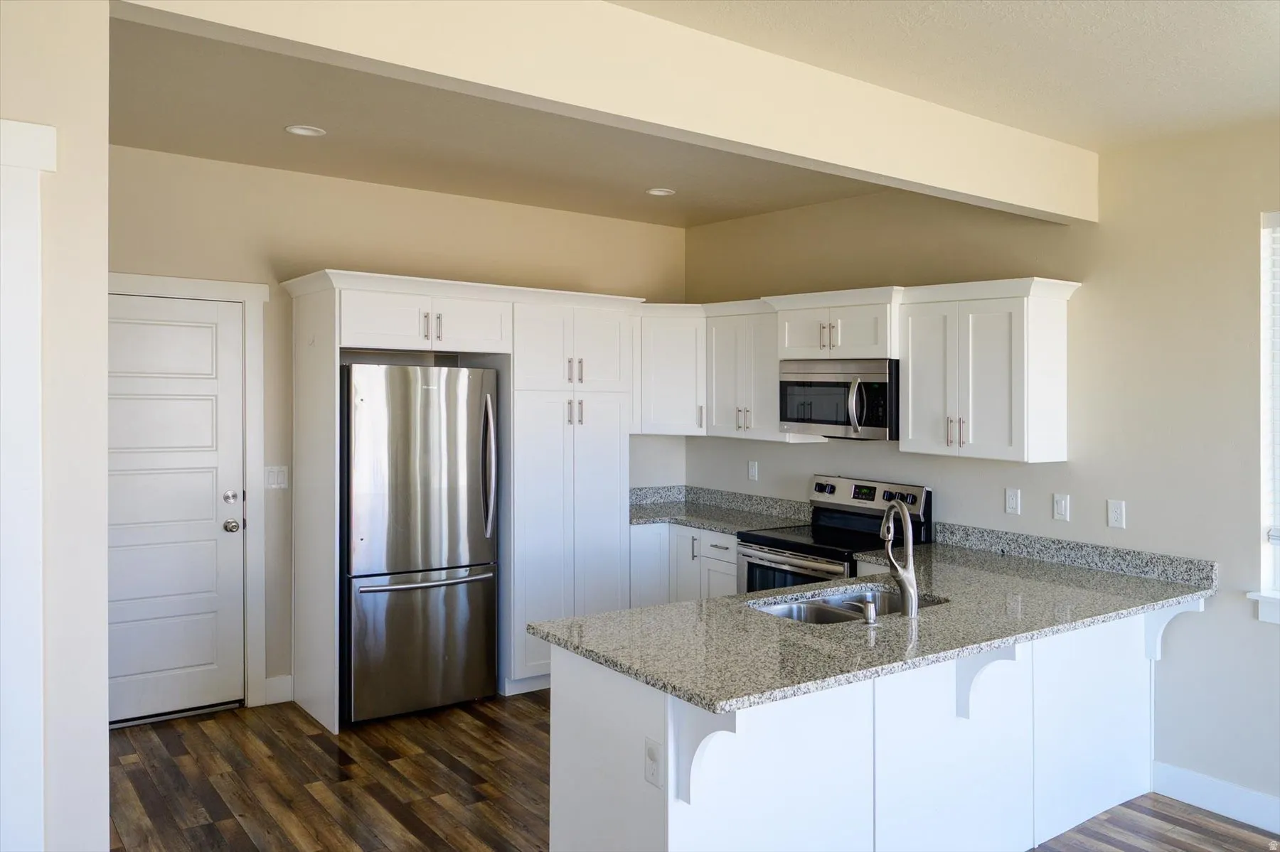 Kitchen featuring light stone counters, a peninsula, stainless steel appliances, white cabinetry, and a kitchen breakfast bar