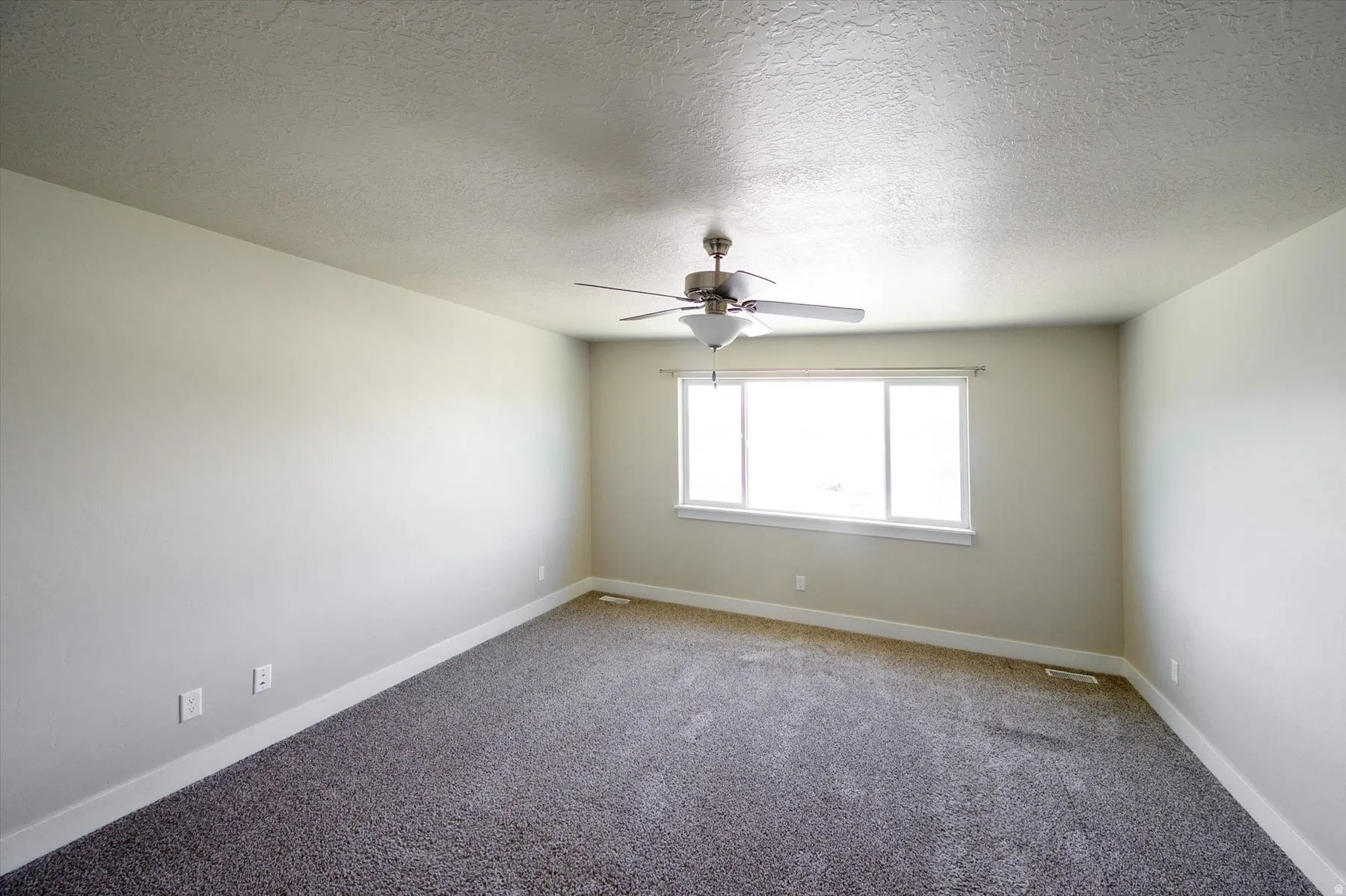 Carpeted empty room featuring a textured ceiling and a ceiling fan