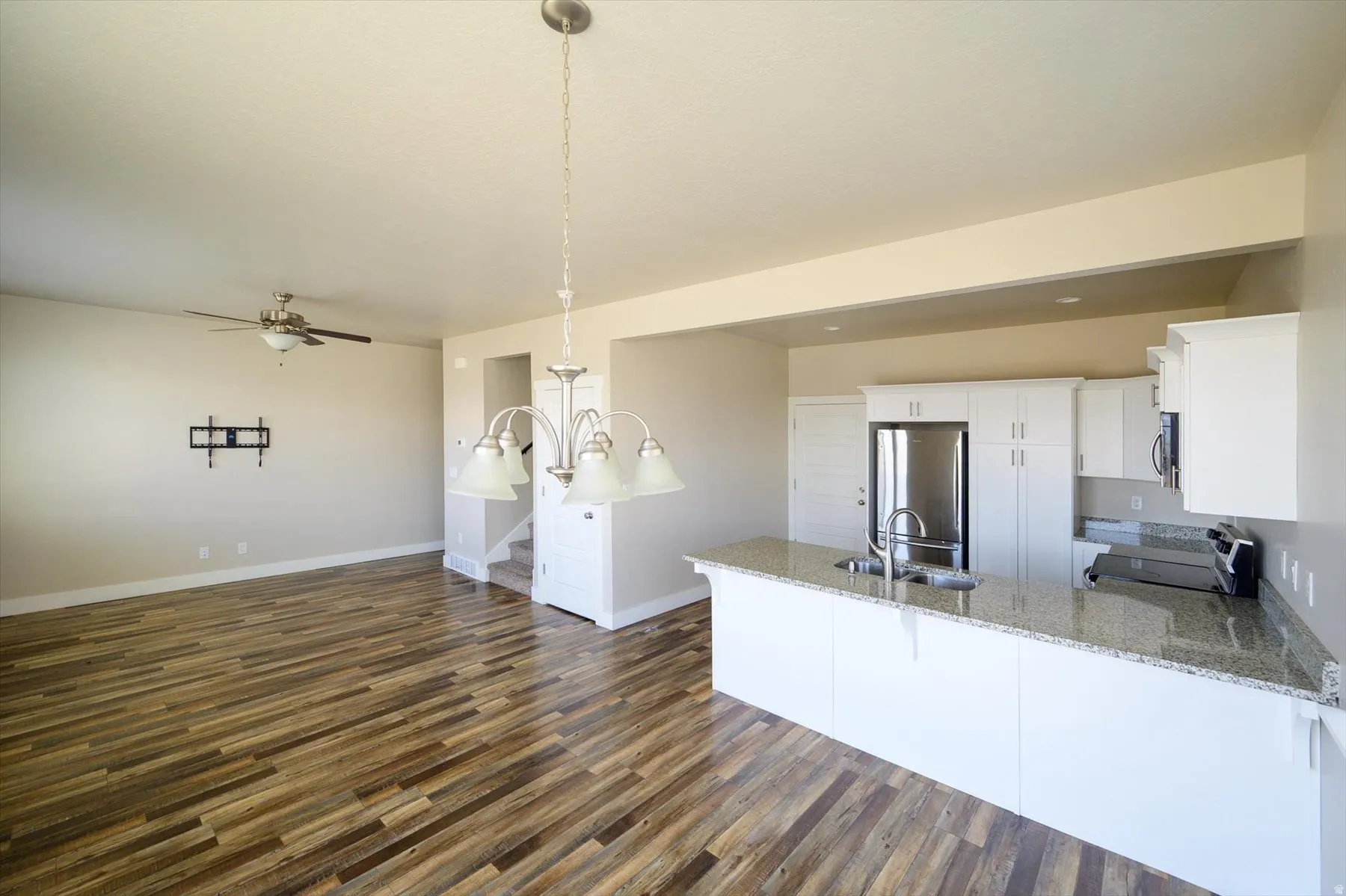 Kitchen with a peninsula, white cabinets, stainless steel appliances, dark wood-style floors, and light stone counters