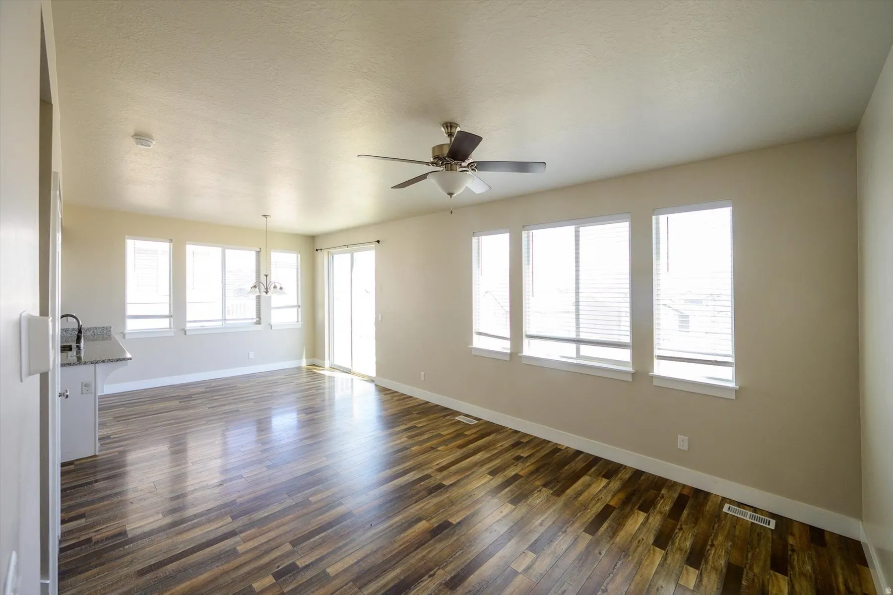 Unfurnished living room featuring ceiling fan, dark wood-style floors, a textured ceiling, and suspended lighting