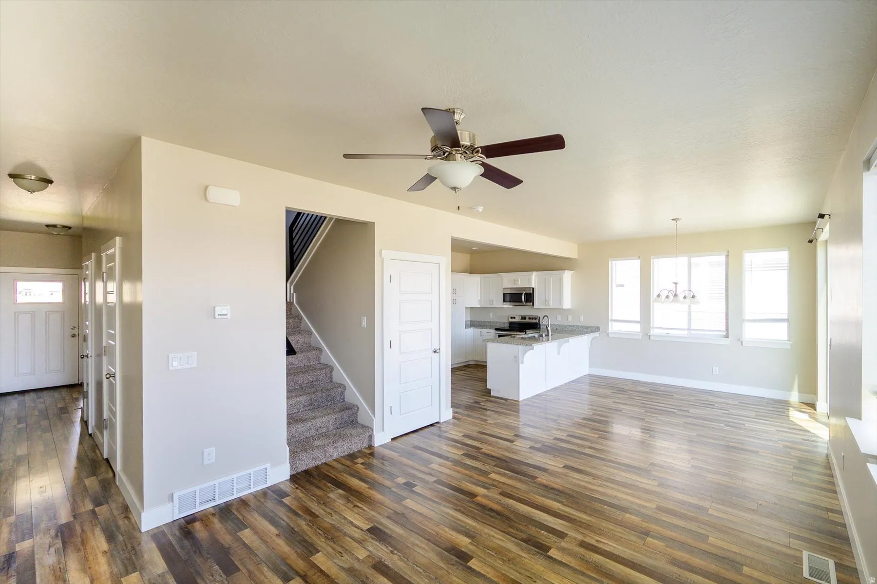 Unfurnished living room featuring dark wood finished floors, a ceiling fan, and suspended lighting