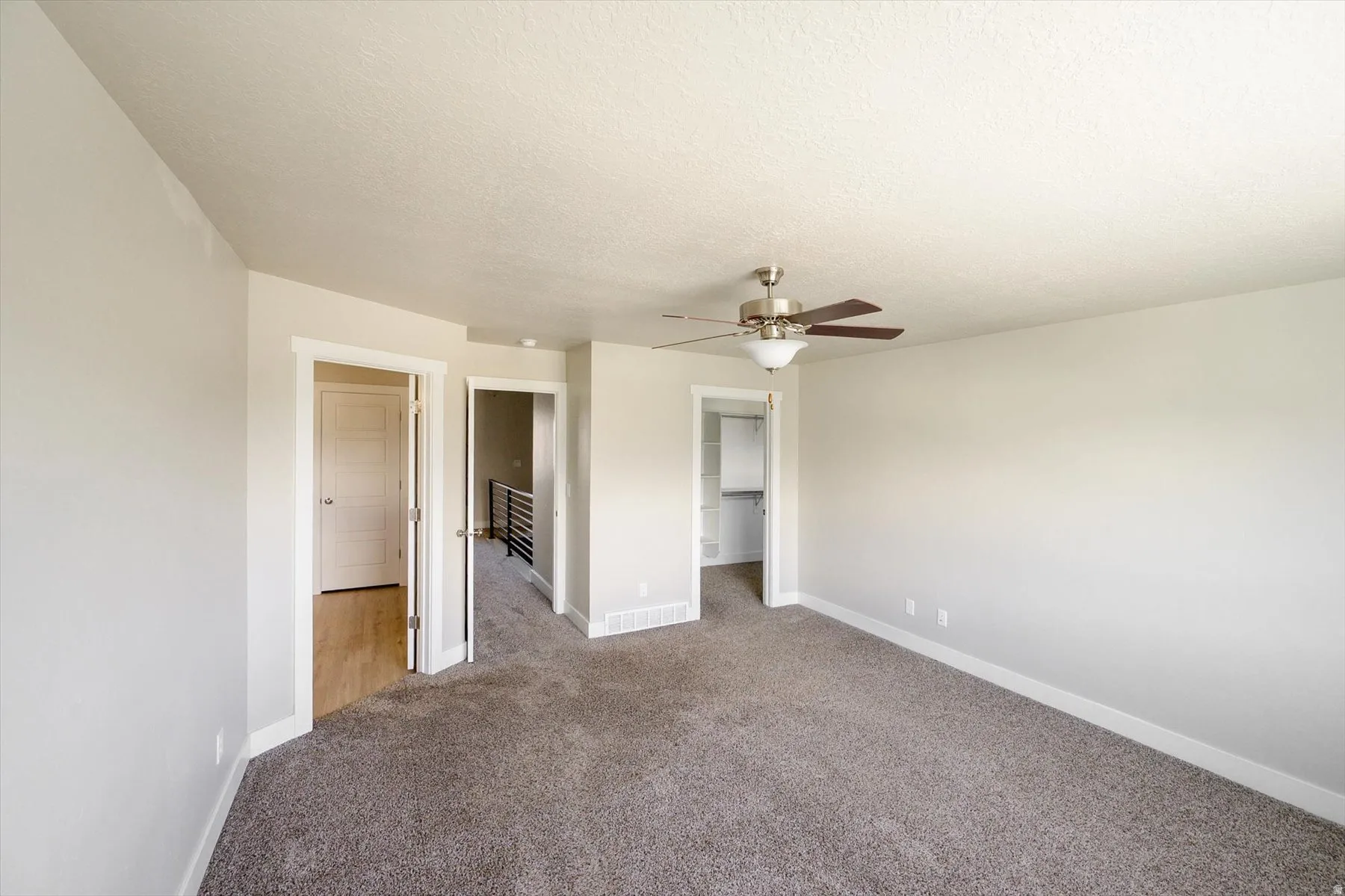 Unfurnished bedroom with a spacious closet, carpet, ceiling fan, and a textured ceiling