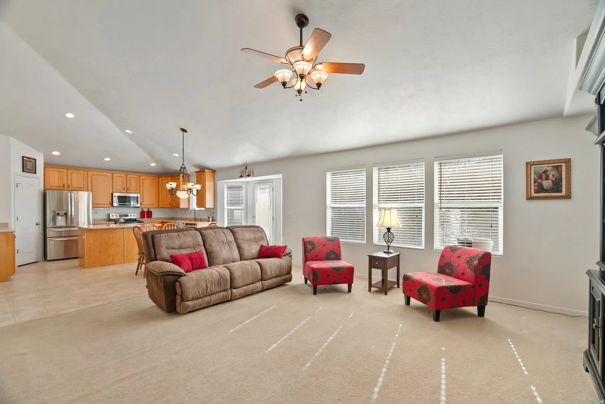 Living area featuring lofted ceiling, healthy amount of natural light, hanging lights, ceiling fan, and light carpet