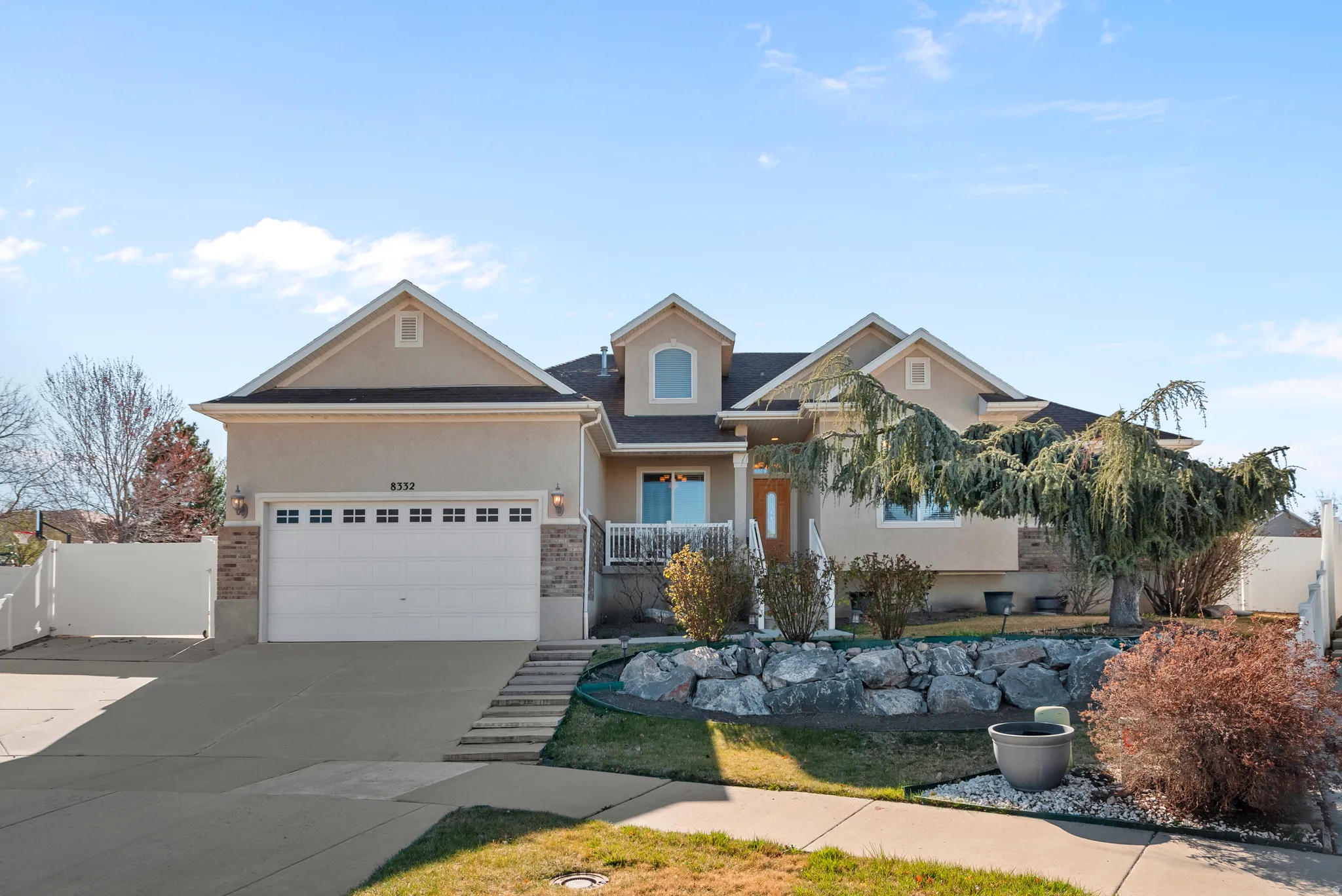 View of front of house with stucco siding, an attached garage, driveway, brick siding, and covered porch