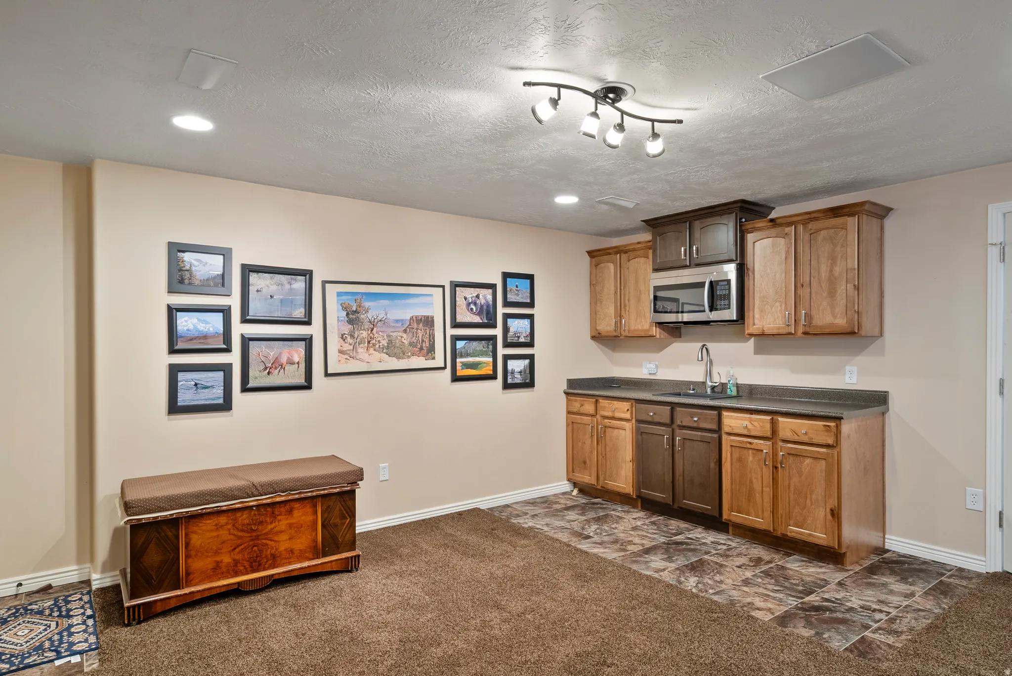 Kitchen featuring dark countertops, wood finish cabinetry, stainless steel microwave, dark carpet, and a textured ceiling