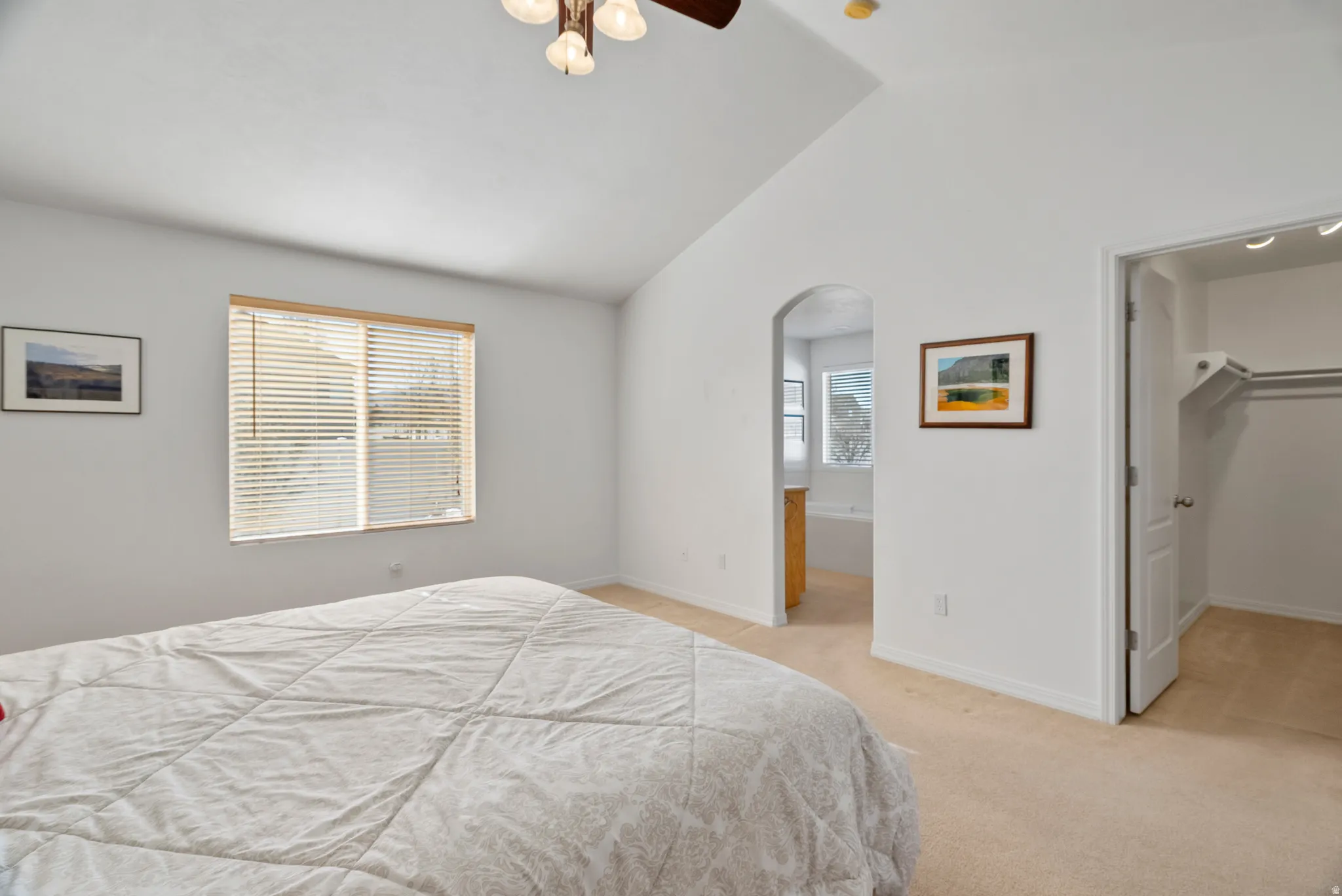 Bedroom with vaulted ceiling, a spacious closet, light carpet, arched walkways, and a ceiling fan