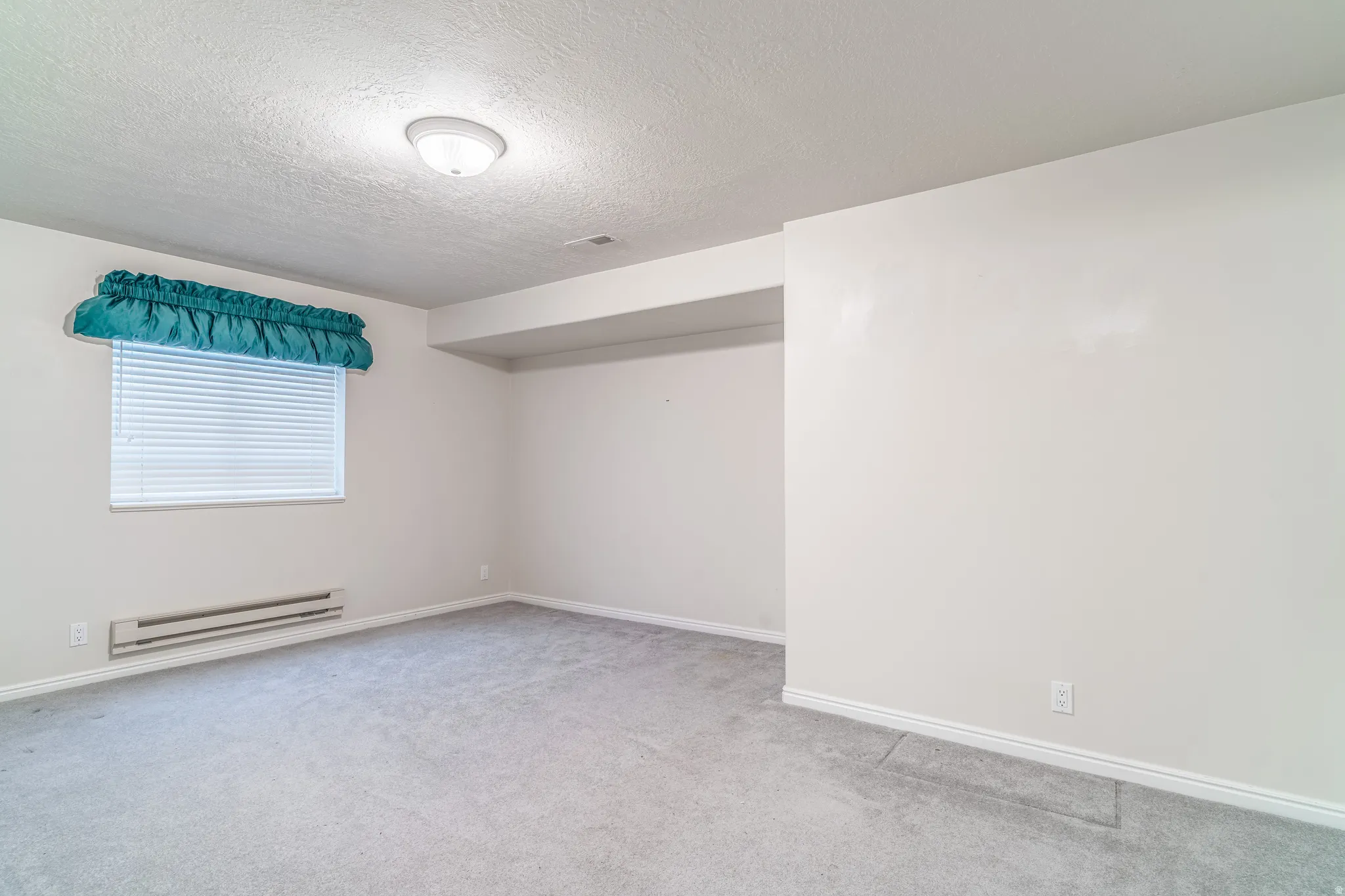 Unfurnished room with a textured ceiling, baseboard heating, and light colored carpet
