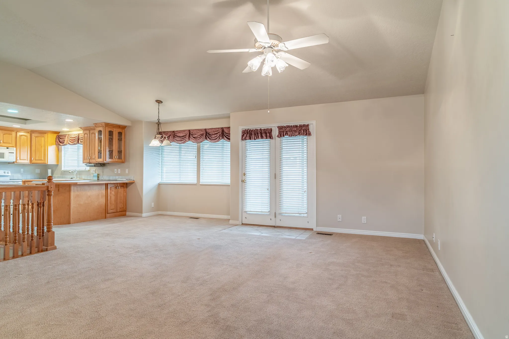 Unfurnished living room with lofted ceiling, a ceiling fan, and light colored carpet