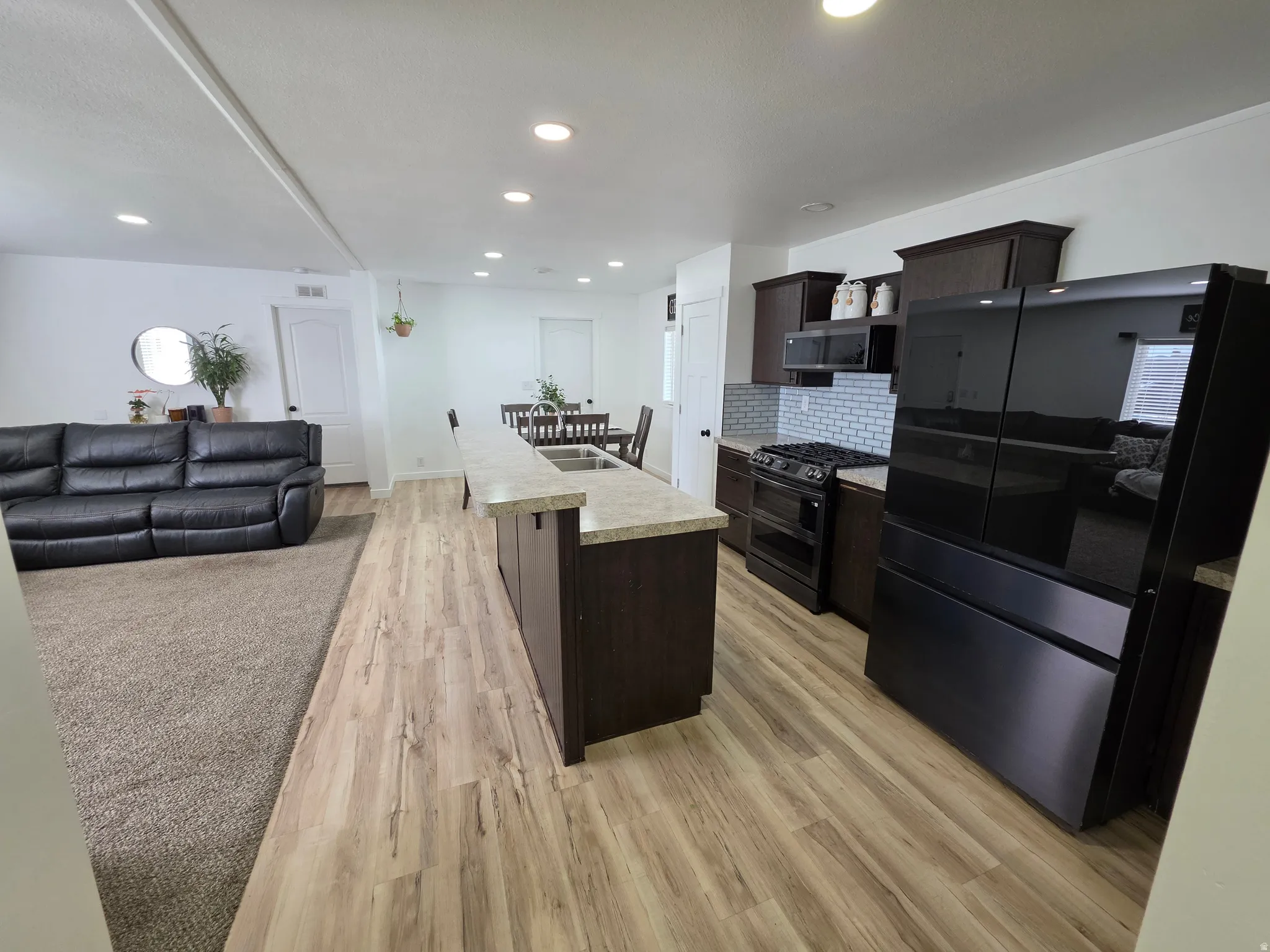 Kitchen featuring dark wood finish cabinets, freestanding refrigerator, light countertops, open floor plan, and a breakfast bar area