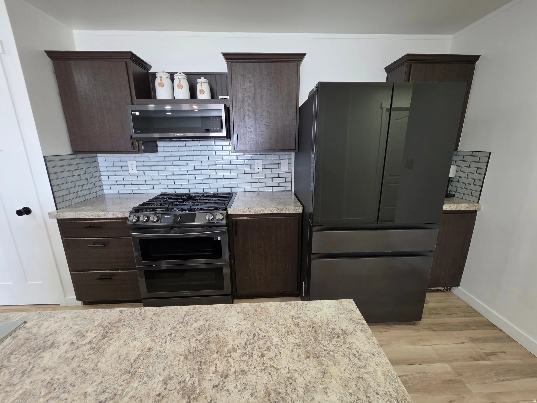 Kitchen with dark wood finish cabinetry, double oven range, extractor fan, freestanding refrigerator, and decorative backsplash