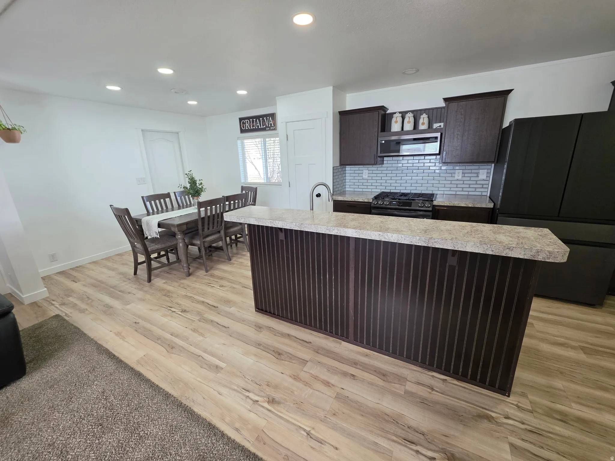 Kitchen with dark wood finish cabinets, light countertops, freestanding refrigerator, decorative backsplash, and range with gas cooktop