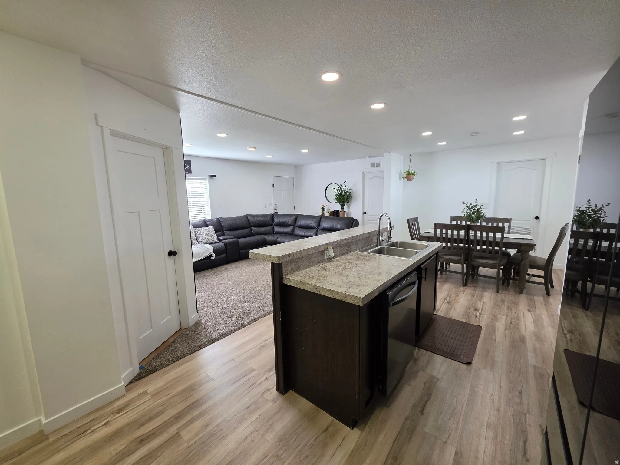 Kitchen featuring open floor plan, light countertops, a kitchen island with sink, light wood finished floors, and stainless steel dishwasher