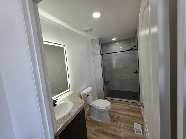 Full bath featuring a shower stall, vanity, wood finished floors, and recessed lighting