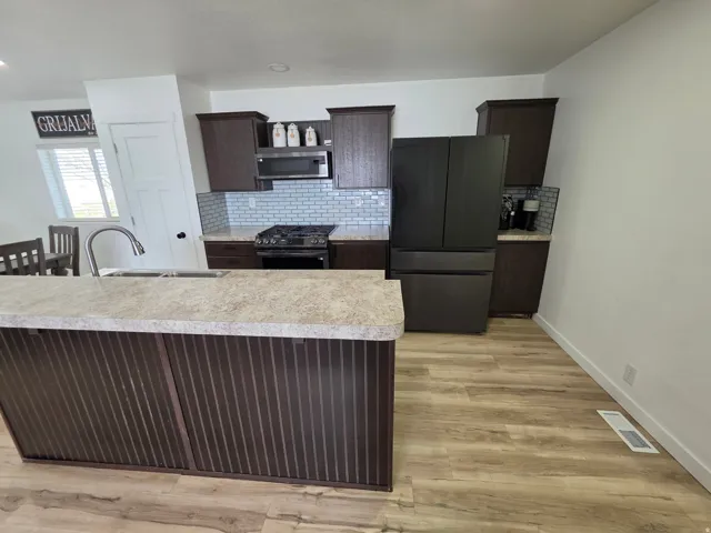 Kitchen featuring dark wood finish cabinetry, stainless steel appliances, light countertops, light wood-type flooring, and decorative backsplash