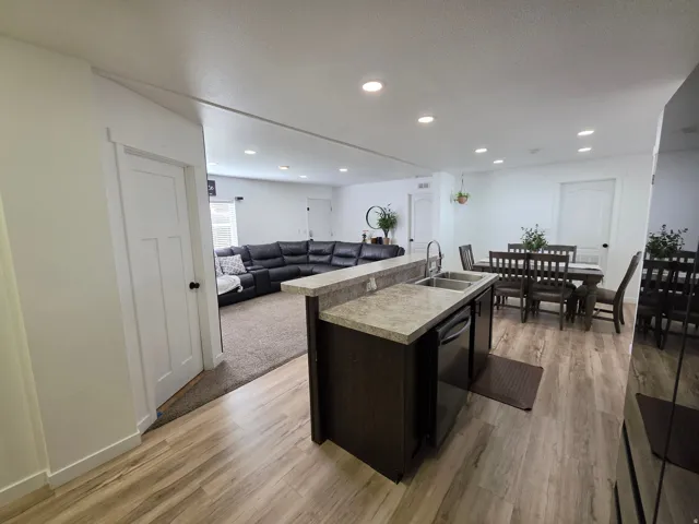 Kitchen featuring open floor plan, light countertops, a kitchen island with sink, light wood finished floors, and stainless steel dishwasher