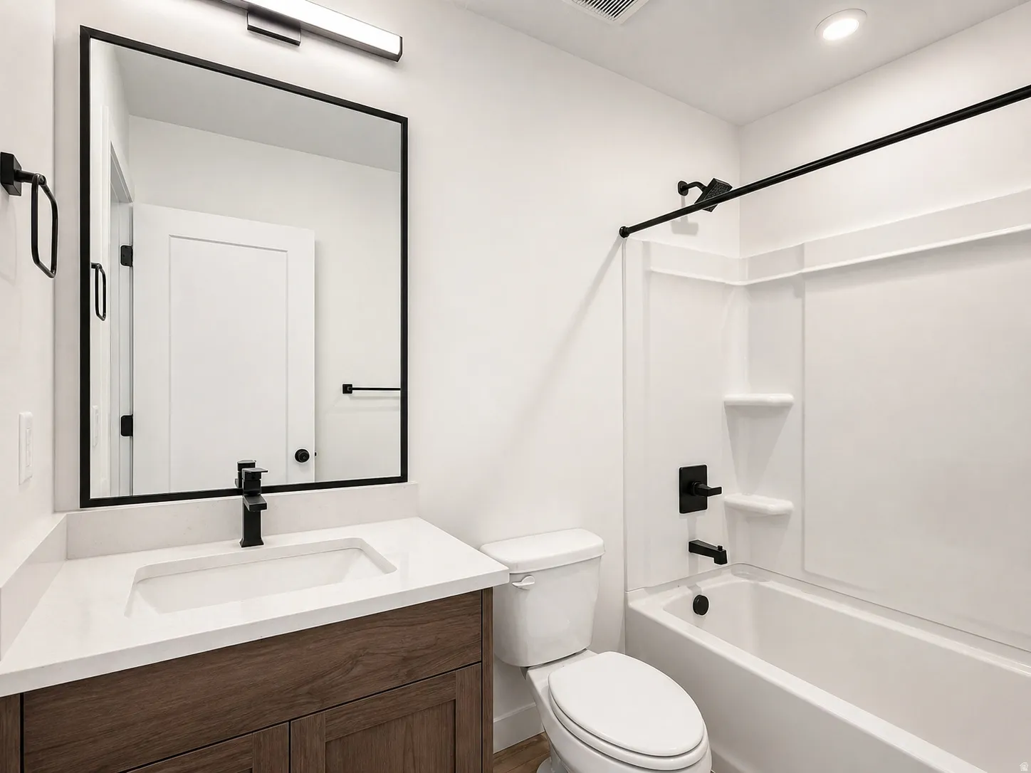 Bathroom featuring a wood-finish vanity with a white countertop and integrated sink, matte black faucet, and a large framed mirror