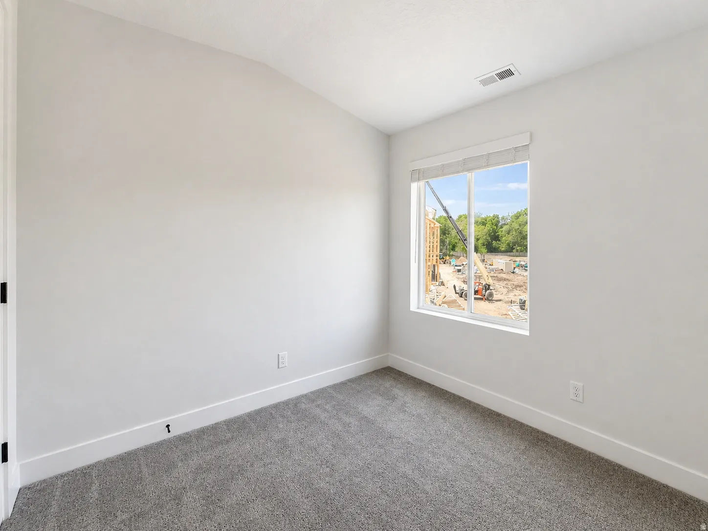 Bright room featuring a large window with white trim, gray plush carpet, white walls, and contemporary baseboards