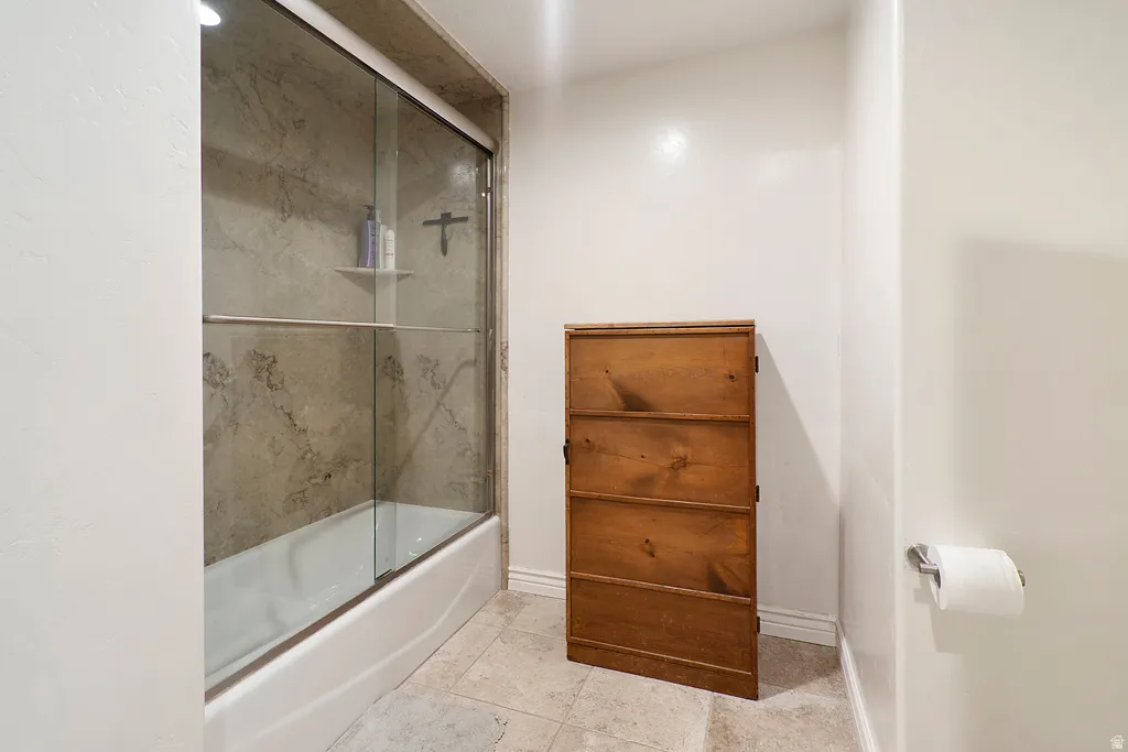 Bathroom featuring combined bath / shower with glass door and light tile patterned flooring