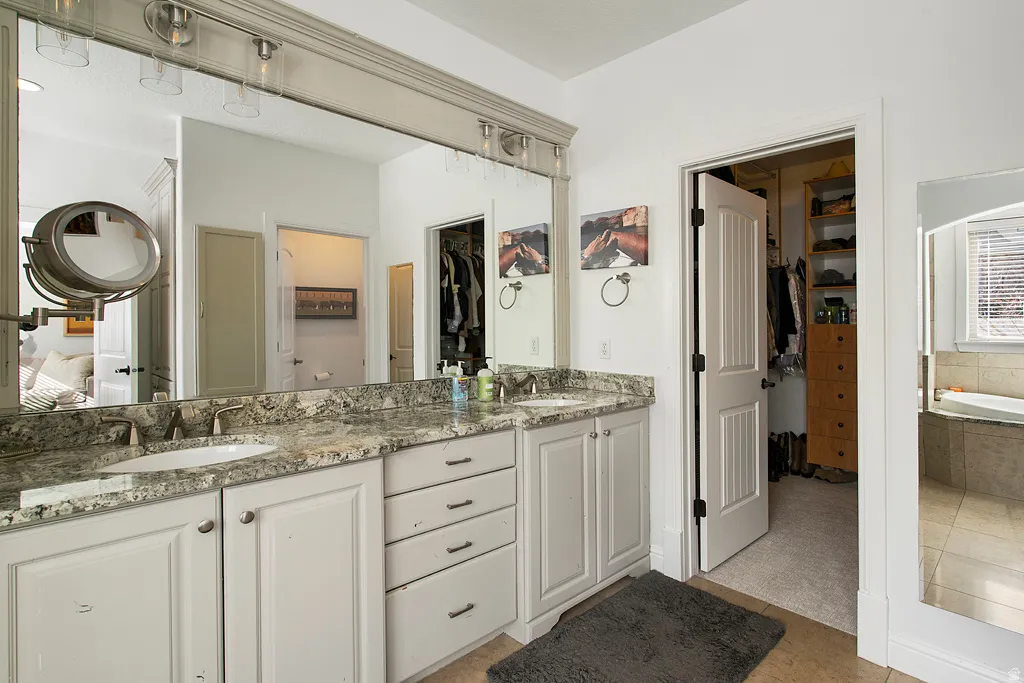 Full bath with a spacious closet, double vanity, a garden tub, and light tile patterned flooring