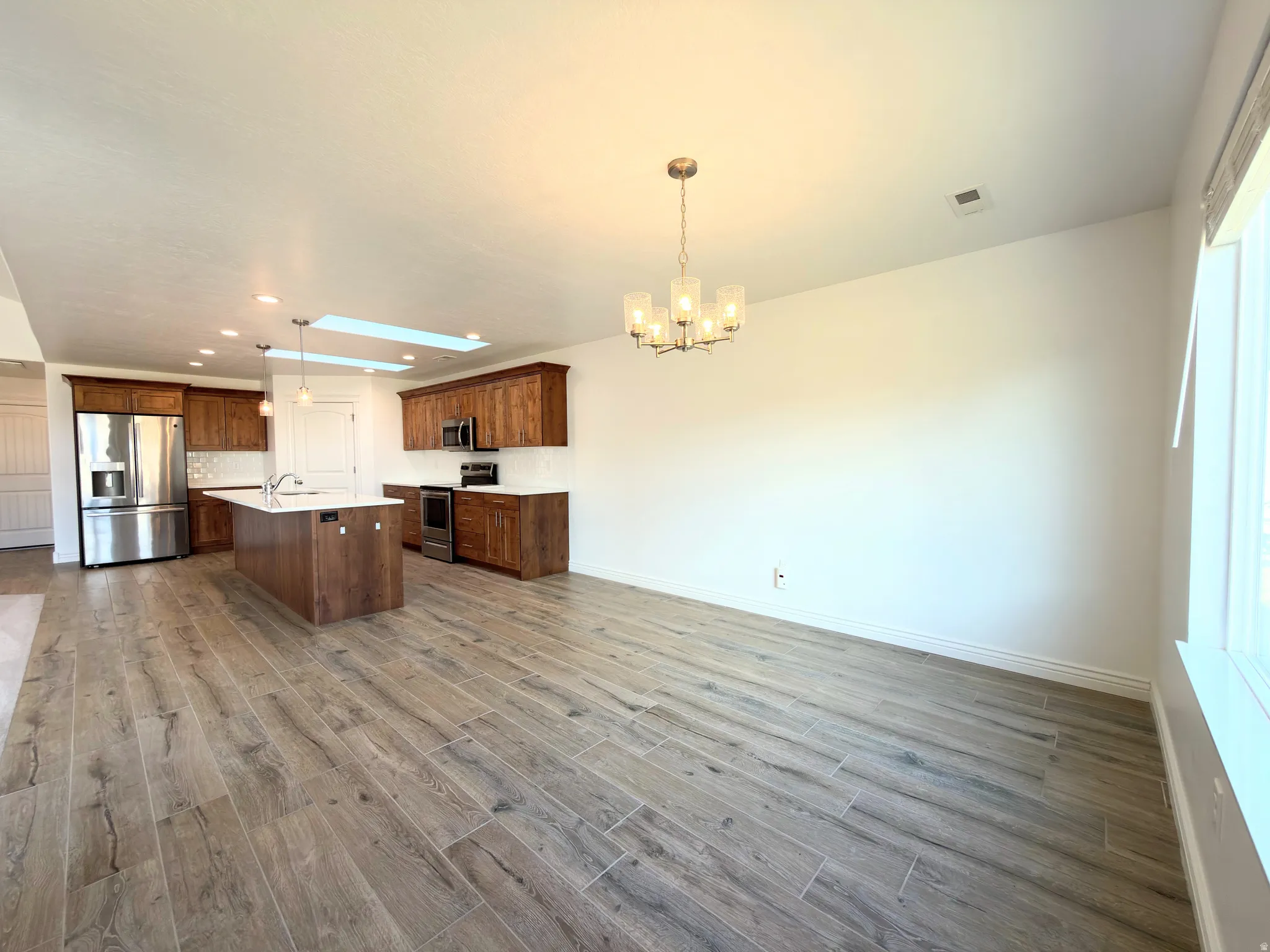 Kitchen with stainless steel appliances, light wood-type flooring, a skylight, an island with sink, and suspended lighting