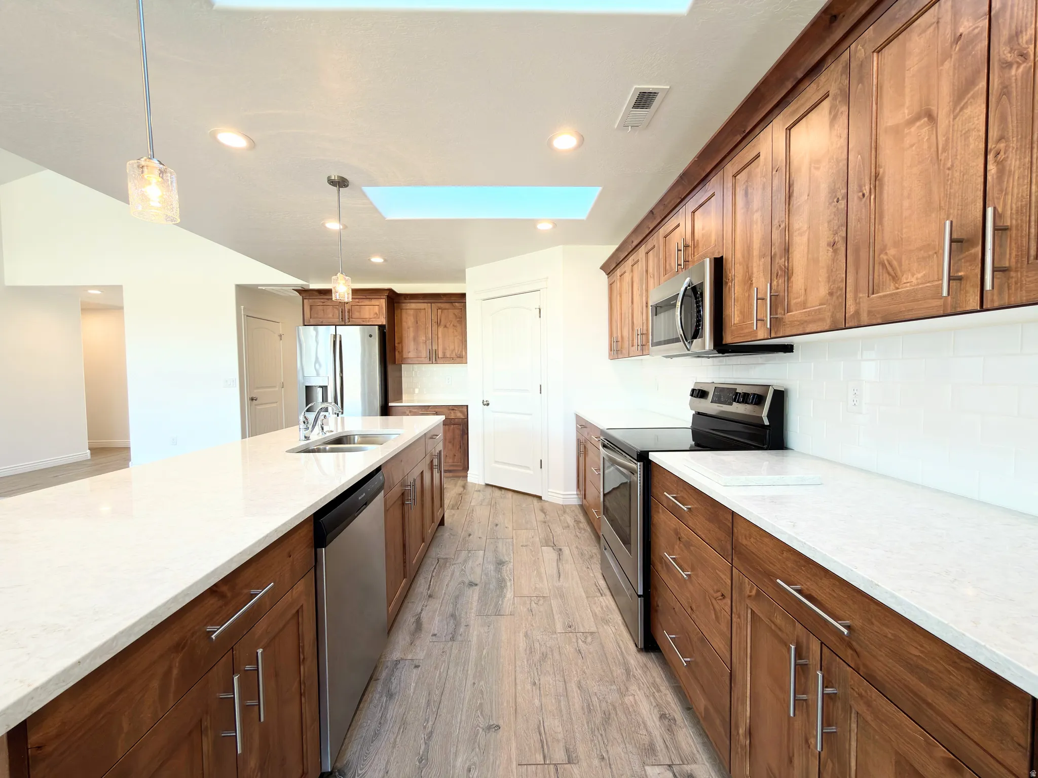 Kitchen featuring stainless steel appliances, light wood-style floors, hanging light fixtures, backsplash, and a skylight