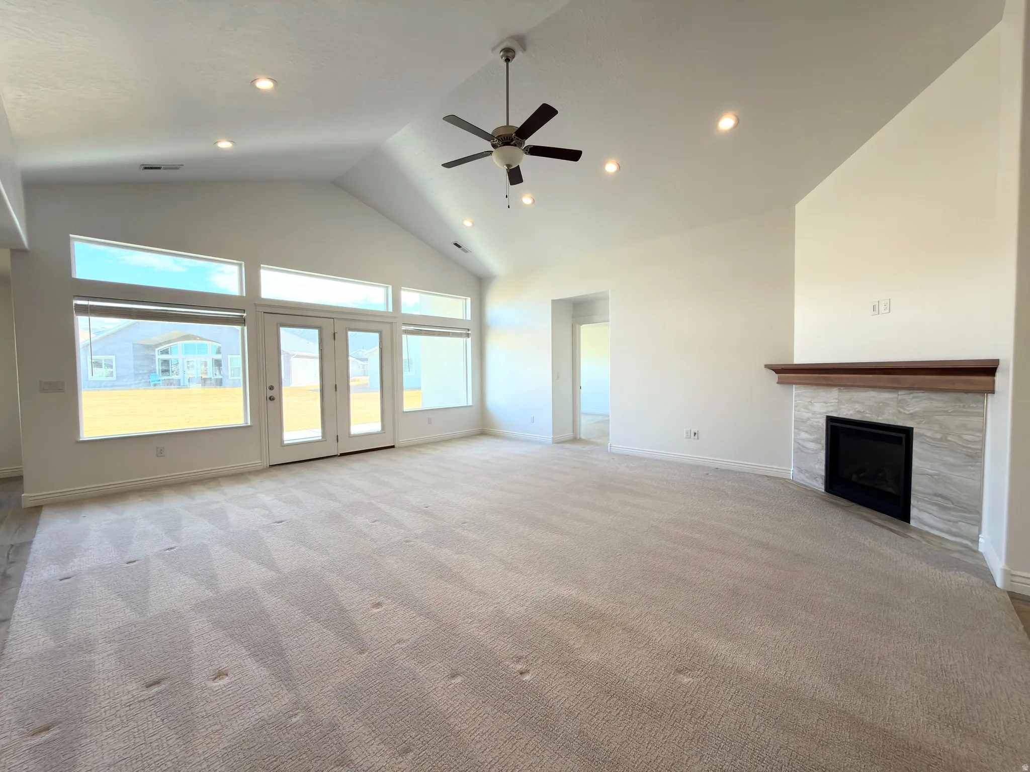 Unfurnished living room featuring a high ceiling, ceiling fan, a fireplace, recessed lighting, and light colored carpet