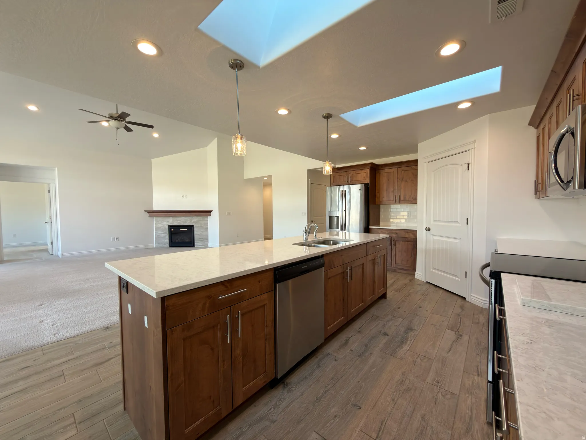 Kitchen featuring a skylight, stainless steel appliances, a tiled fireplace, decorative light fixtures, and an island with sink