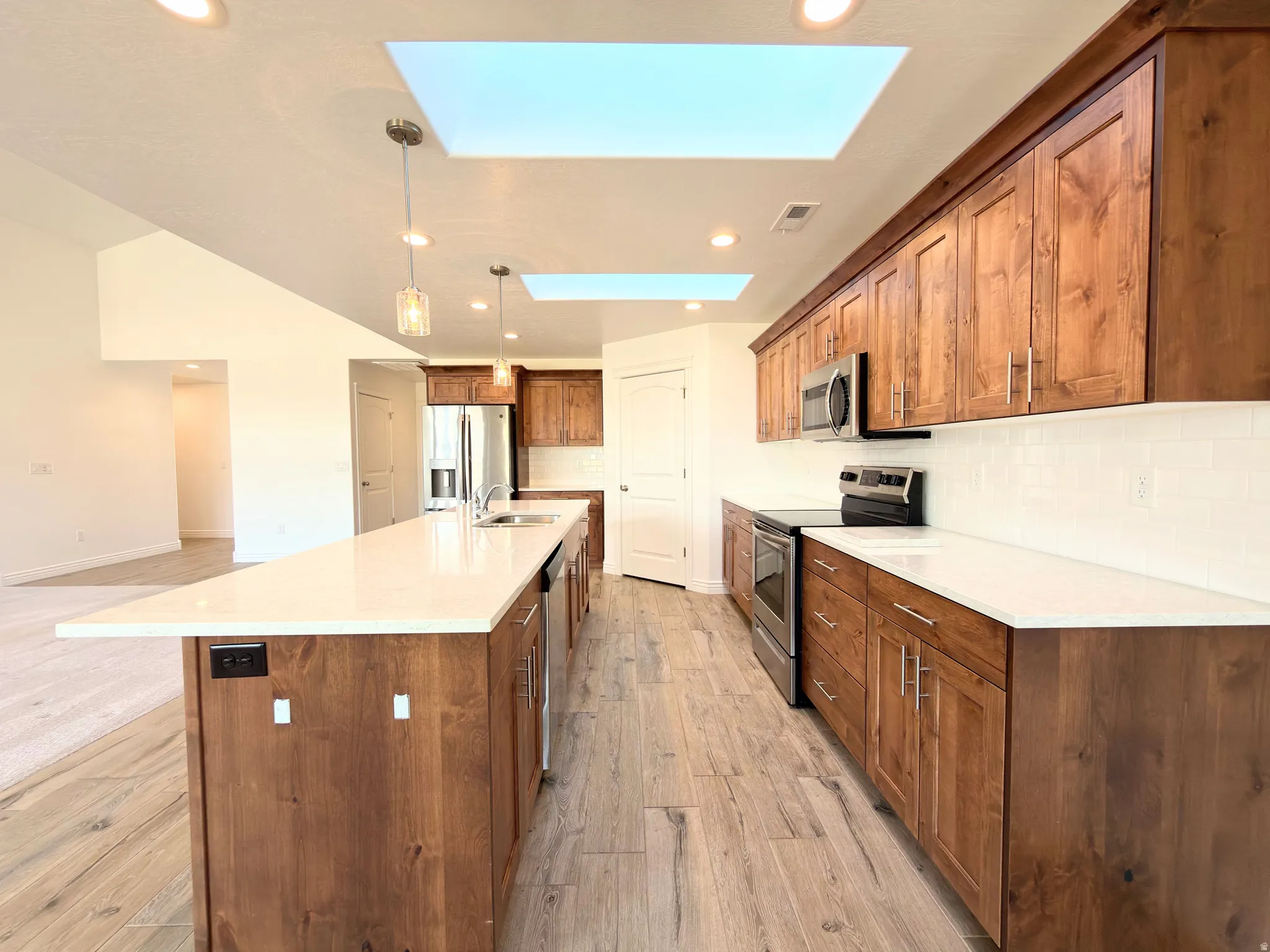 Kitchen with a skylight, stainless steel appliances, wood finish cabinetry, light wood finished floors, and decorative backsplash