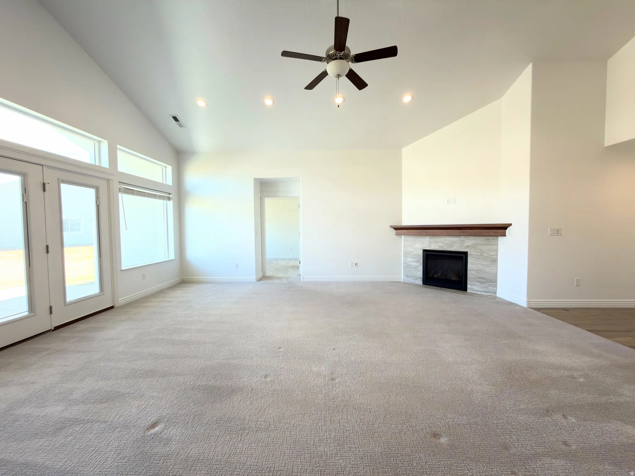 Unfurnished living room with ceiling fan, a tiled fireplace, lofted ceiling, recessed lighting, and light colored carpet