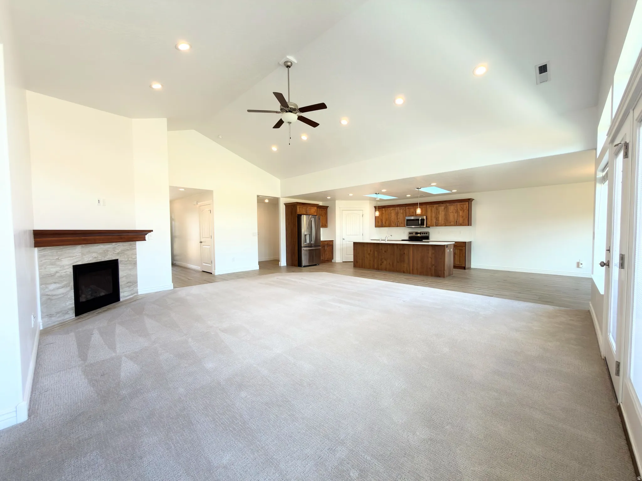 Unfurnished living room featuring light colored carpet, a premium fireplace, a ceiling fan, vaulted ceiling, and recessed lighting