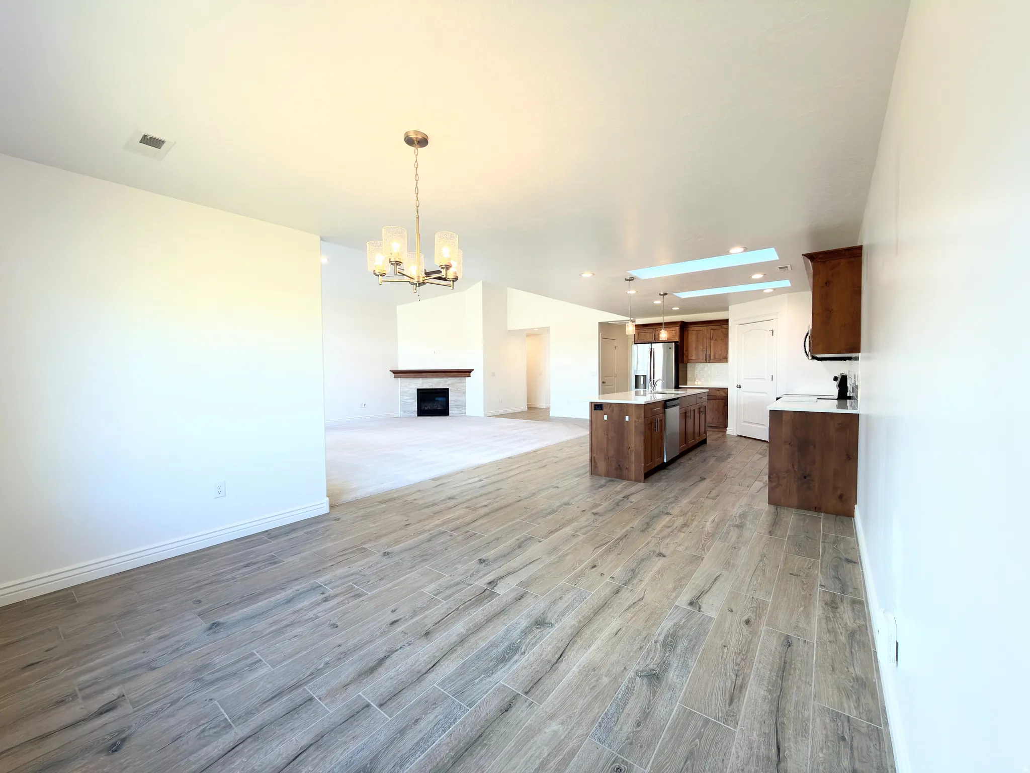 Kitchen featuring open floor plan, a center island with sink, hanging lights, a fireplace, and stainless steel appliances