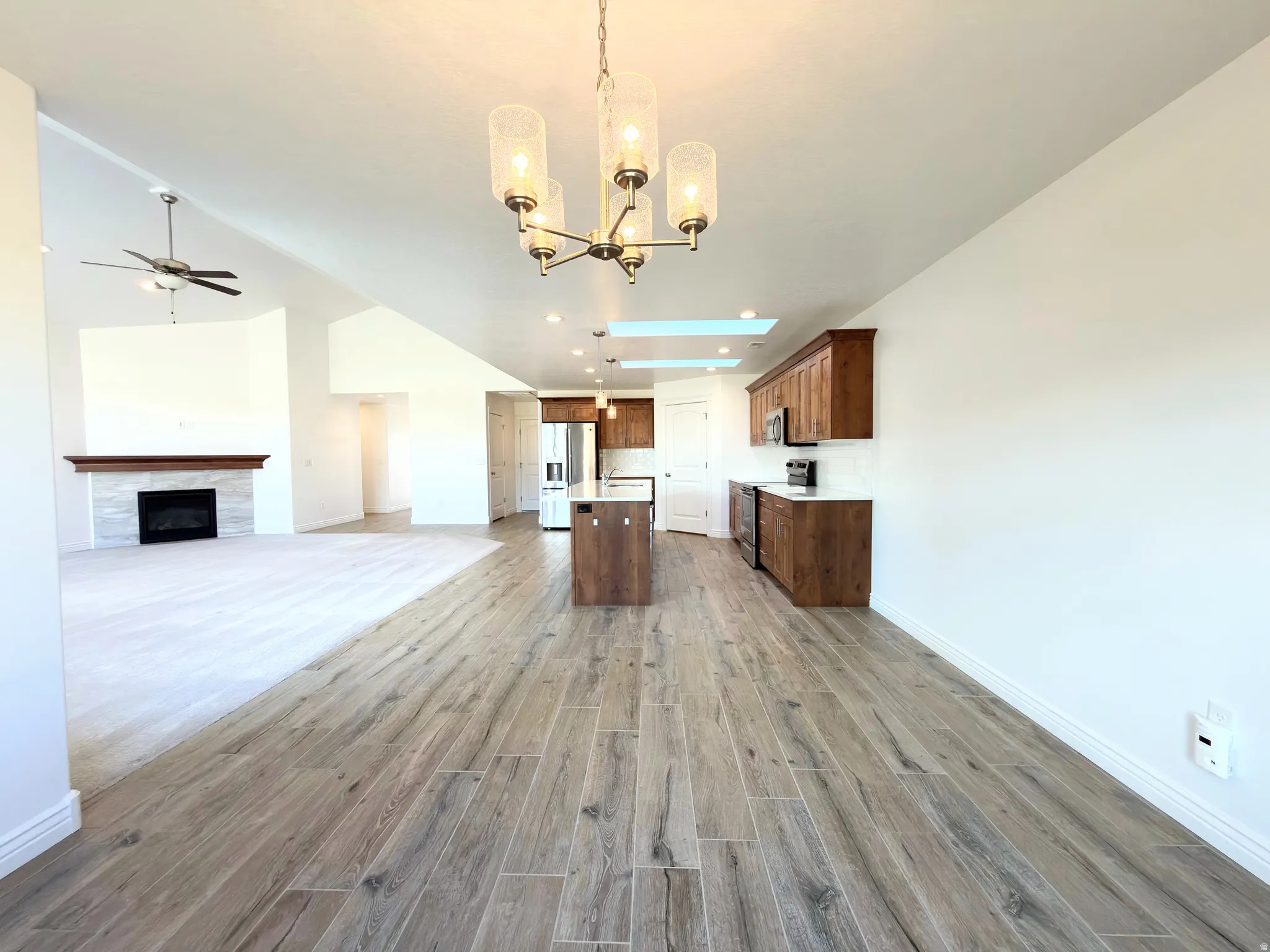 Kitchen with open floor plan, a kitchen island with sink, a tiled fireplace, ceiling fan, and light wood-style floors
