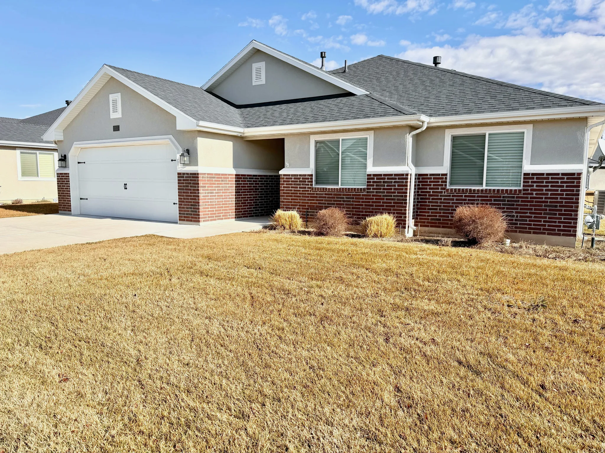 View of front of house with a front lawn, brick siding, a garage, and stucco siding