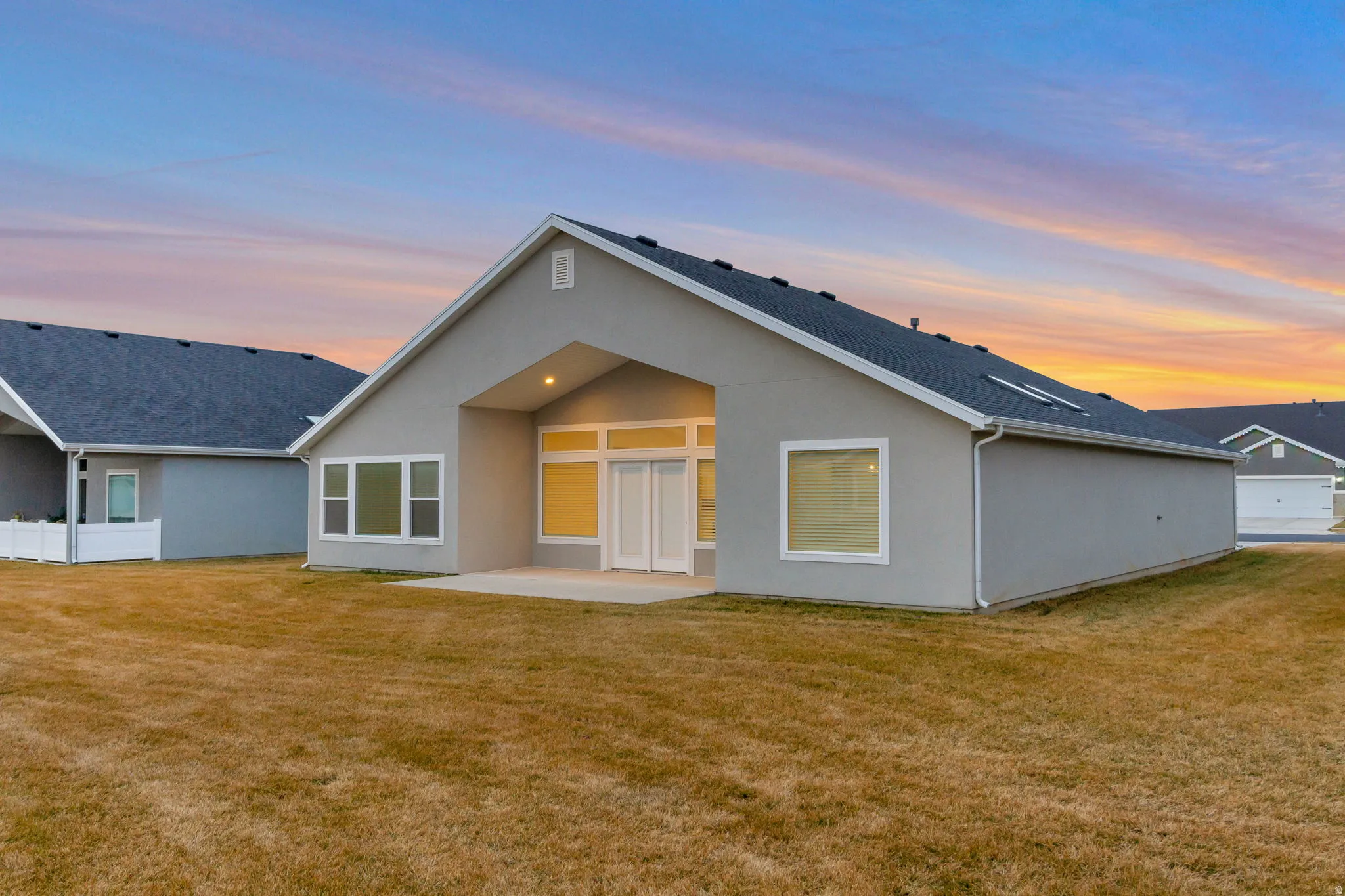 Rear view of house with a patio area, a lawn, and stucco siding