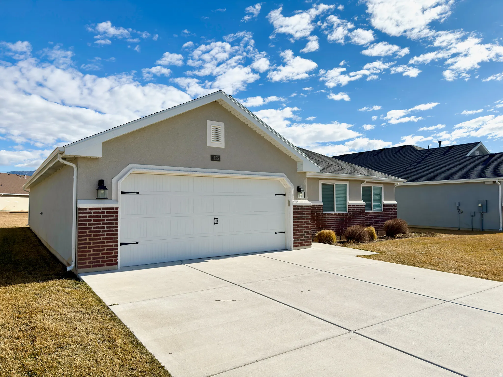 Ranch-style home featuring brick siding, concrete driveway, an attached garage, a front yard, and stucco siding