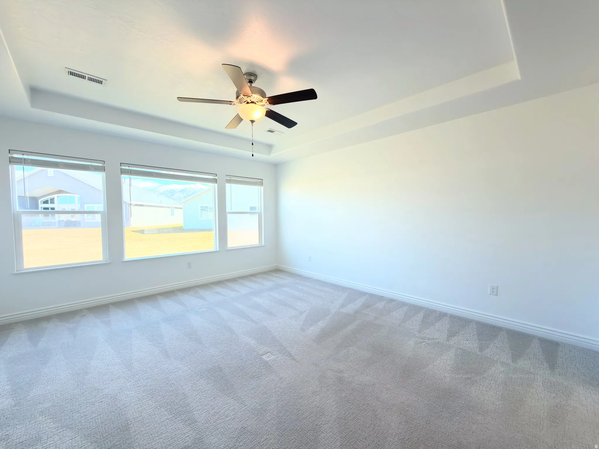 Carpeted empty room featuring a tray ceiling and ceiling fan